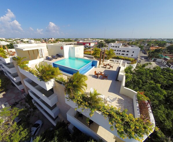 Una piscina en la azotea con vistas a la ciudad, rodeada de vegetación y edificios modernos.