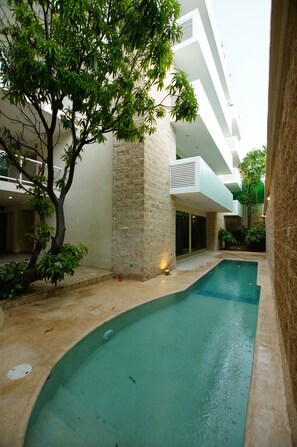 A swimming pool with a stone wall and a tree in a courtyard. - Hotel Angelo's (Playa del Carmen)