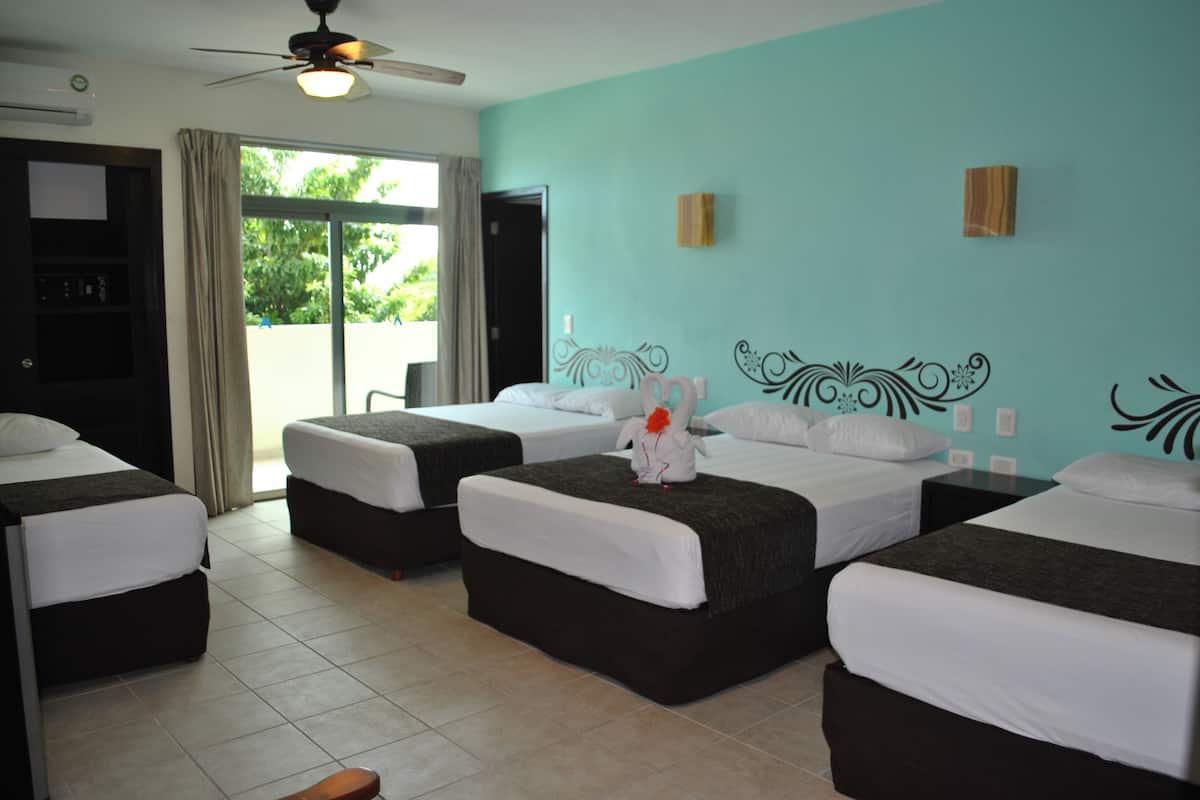 A hotel room with four beds, a ceiling fan, and a view of greenery outside.
