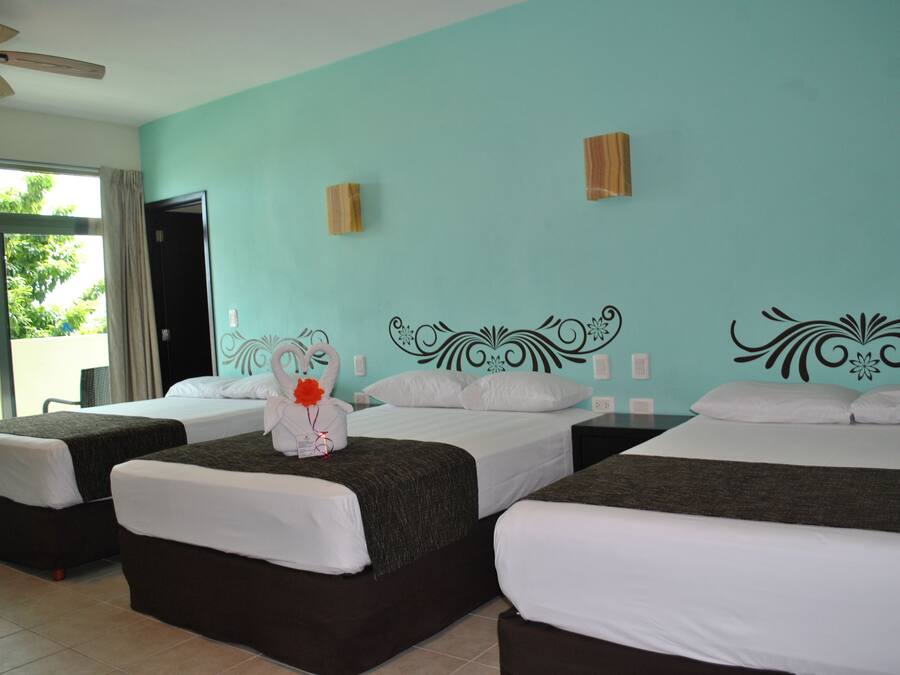 A hotel room with three beds, a large window, and a teal-colored wall.