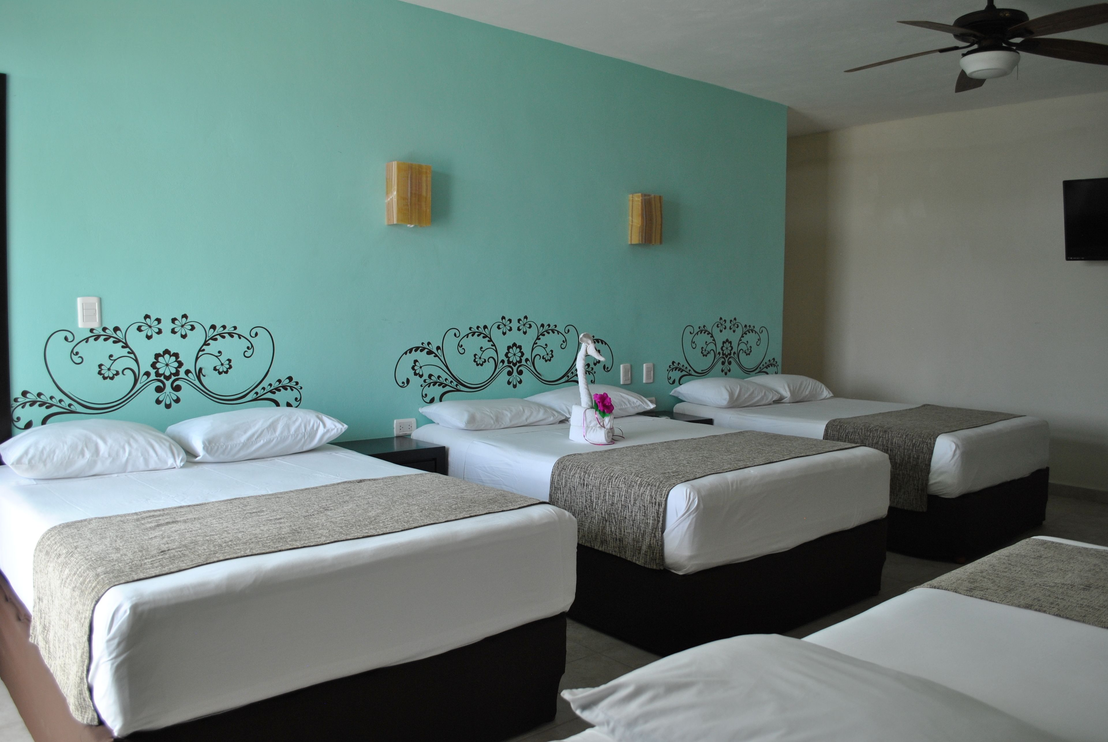 Une chambre d’hôtel avec quatre lits simples, un ventilateur de plafond et des appliques murales décoratives.