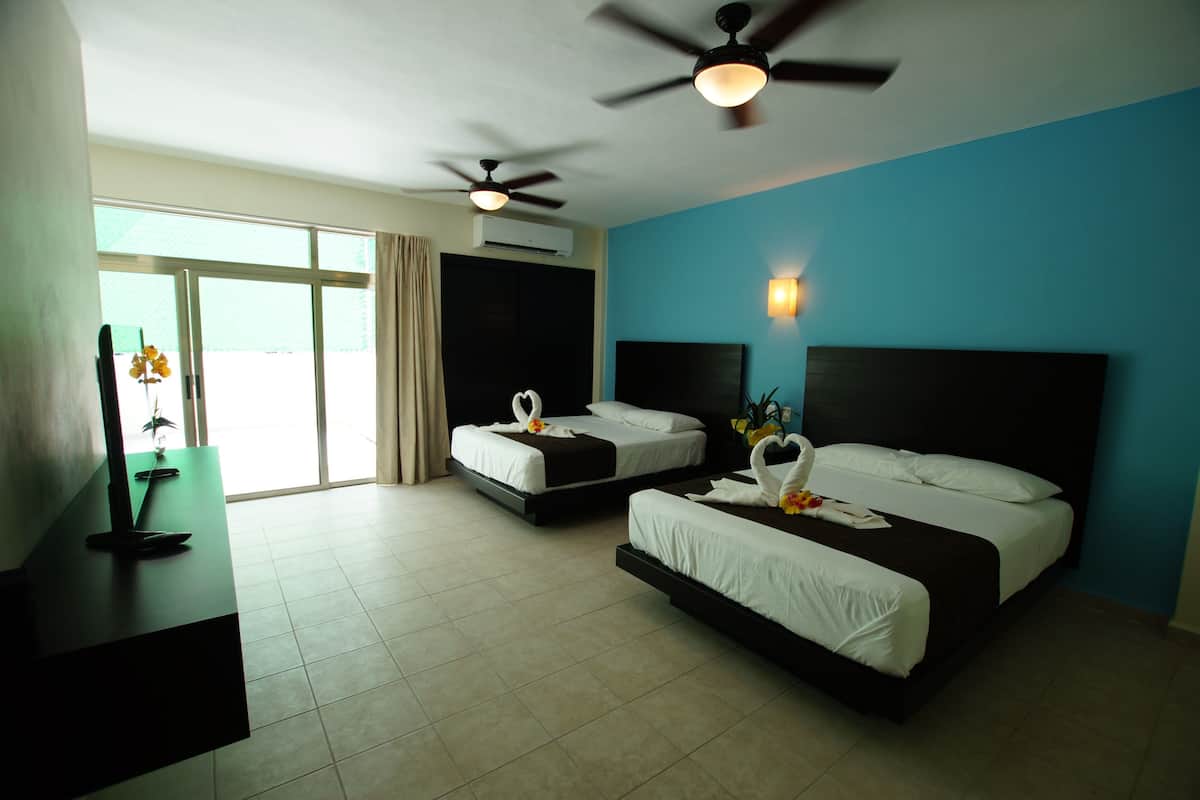 A hotel room with two beds, a desk, a TV, and a ceiling fan.