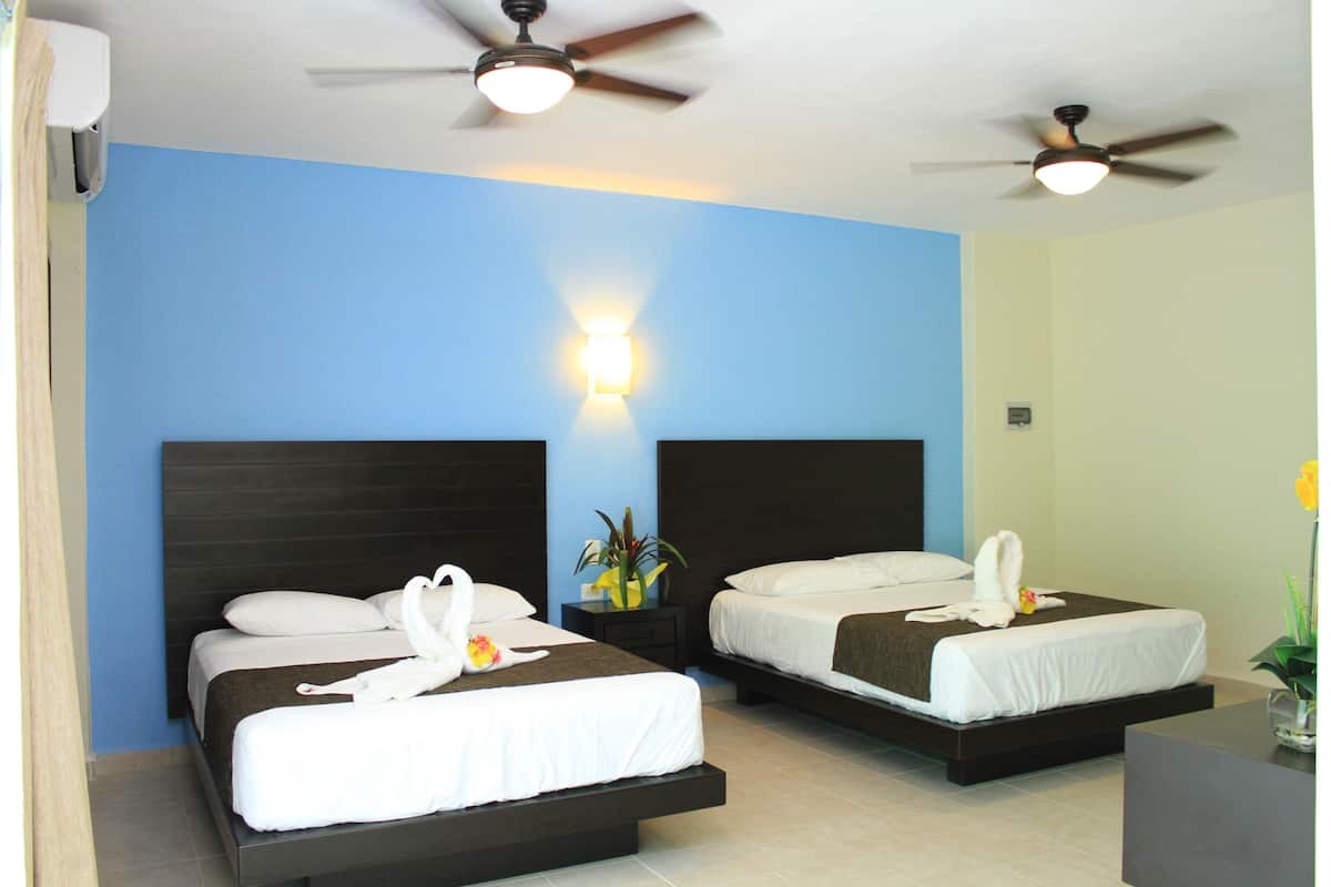 A hotel room with two beds, each with white linens and towels, a nightstand with a vase of flowers, and a ceiling fan.
