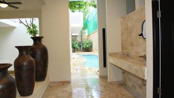 A bathroom with a stone floor, a sink, and a shower. There is a plant in a vase on the wall.