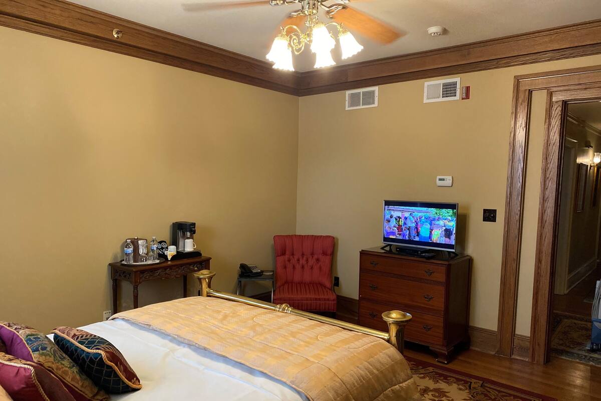 Habitación de hotel con cama, televisor, una mesita de centro, un sillón rojo y un aparador de madera.