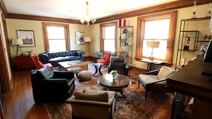 A spacious living room with a black leather sofa, a red armchair, a beige armchair, a coffee table, and a chandelier. - Inn at 835 Boutique Hotel (Springfield)