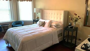 Un dormitorio ordenado con una cama grande, una mesita de noche con lámpara, una silla y una pequeña mesa con un jarrón de flores.
