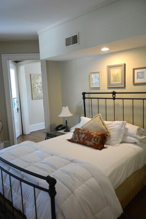 A neatly made bed with white bedding and a floral pillow, a bedside lamp, and framed pictures on the wall.