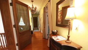A hallway with wooden flooring, a chandelier, a mirror, and a lamp. - Inn at 835 Boutique Hotel (Springfield)