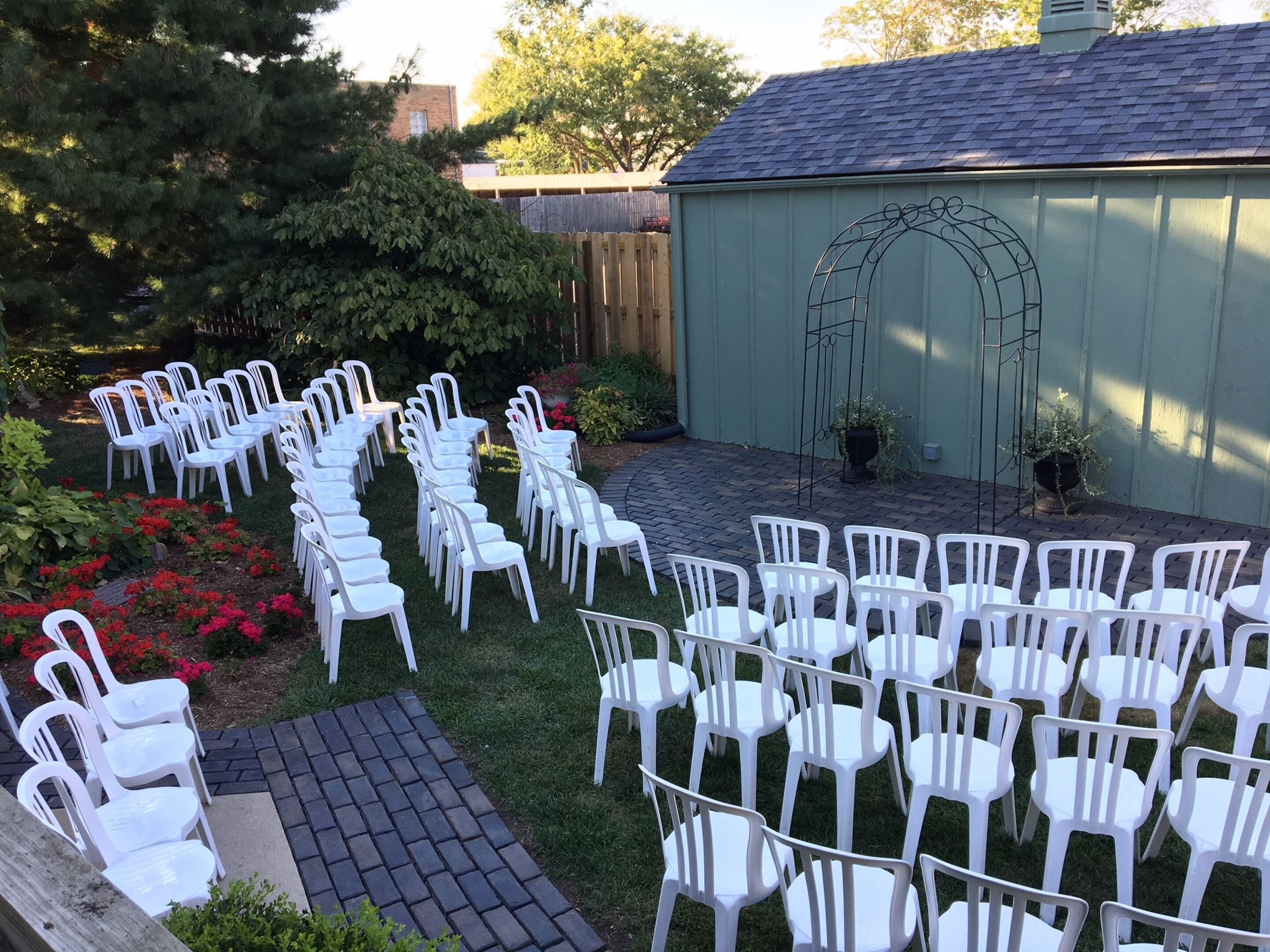 A patio with white plastic chairs arranged in rows, a brick pathway, and a green lawn.