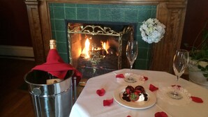 A table set for two with a plate of strawberries and chocolate, a bottle of champagne, and a fireplace in the background. - Inn at 835 Boutique Hotel (Springfield)