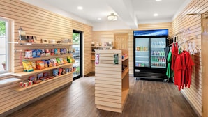 A clean, modern retail space with wooden paneling, shelves stocked with snacks, a beverage refrigerator, and a clothing rack. - Best Western Palmyra Inn & Suites (Palmyra)