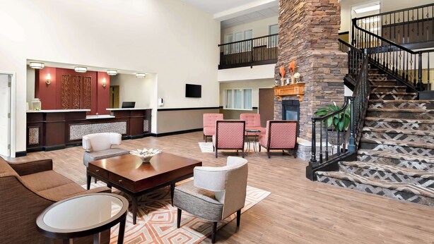 A spacious lobby with a high ceiling, a stone fireplace, and a staircase with a black railing. - Best Western Palmyra Inn & Suites (Palmyra)
