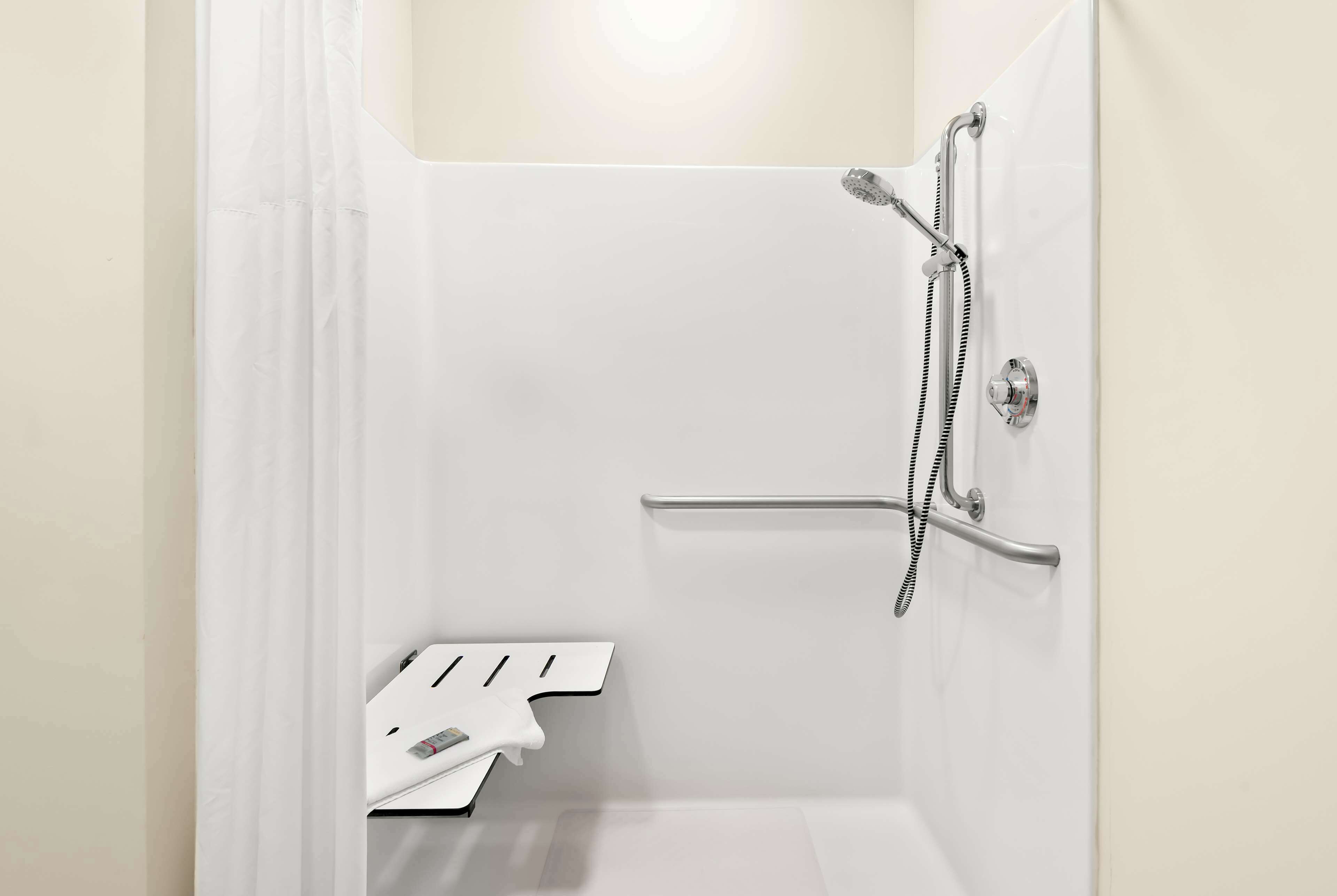 A white shower with a handheld showerhead and a handheld faucet.