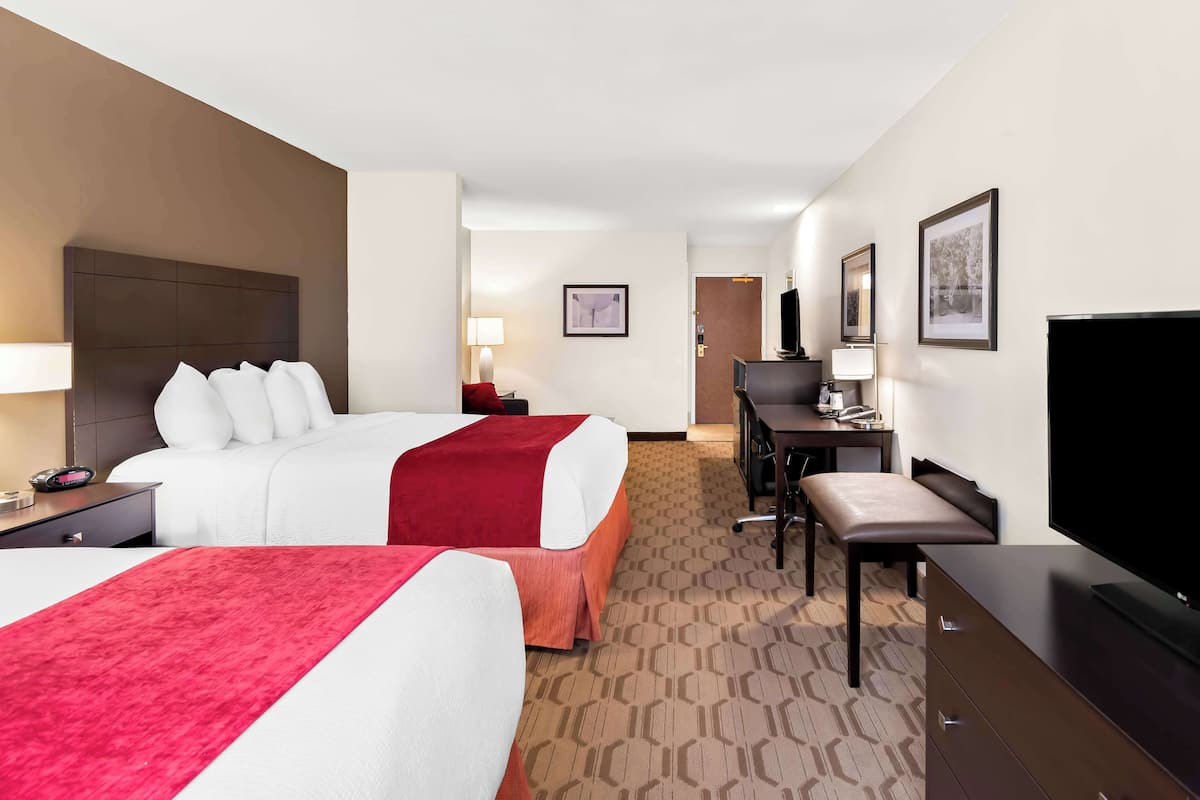 A hotel room with two beds, a desk, a chair, a television, and a desk lamp.