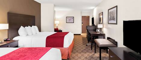 A hotel room with two beds, a desk, a chair, a television, and a desk lamp.