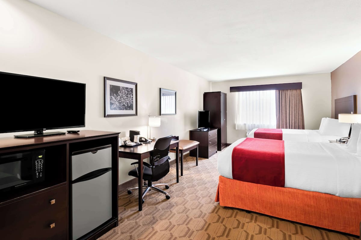 A hotel room with a bed, desk, chair, television, and a minibar.