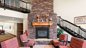 A lobby with a stone fireplace, red patterned chairs, a patterned rug, and a staircase with black railings. - Best Western Palmyra Inn & Suites (Palmyra)
