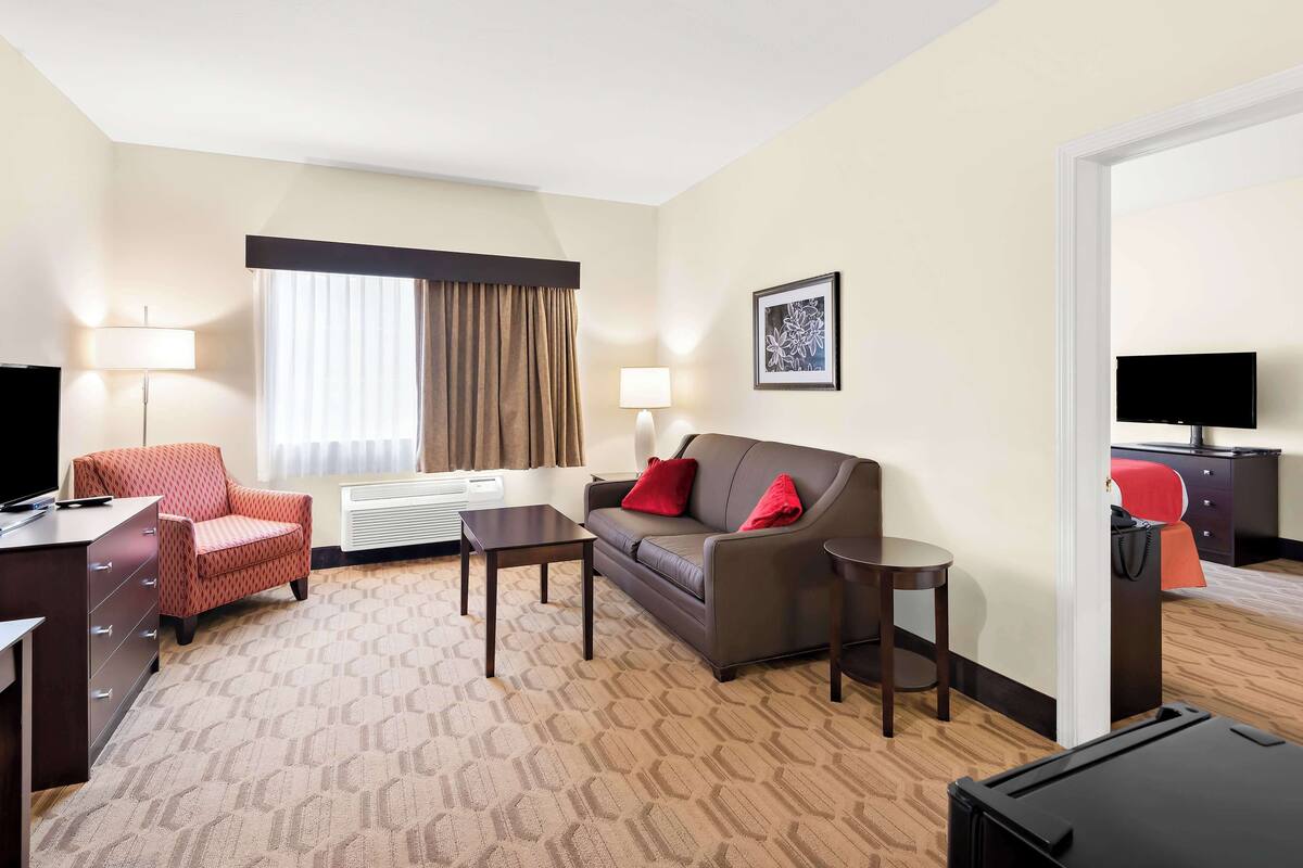 A hotel room with a sofa, armchair, desk, and a flat-screen TV.