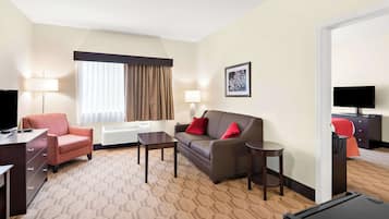 Habitación de hotel con sofá, sillón, escritorio y televisión de pantalla plana.