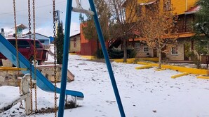 A swing set in a snowy outdoor area with a yellow building in the background.