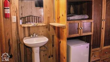 Une salle de bain de style rustique, avec des murs en bois, comprenant un lavabo, un miroir, un extincteur et un petit réfrigérateur.