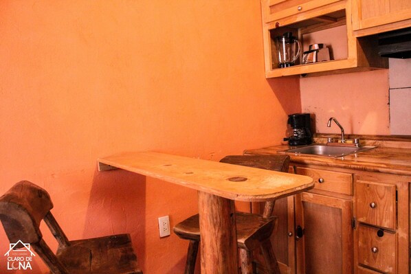 A kitchen with a wooden table, bar stools, a coffee maker, and a sink. - Cabañas Claro De Luna (Bocoyna)