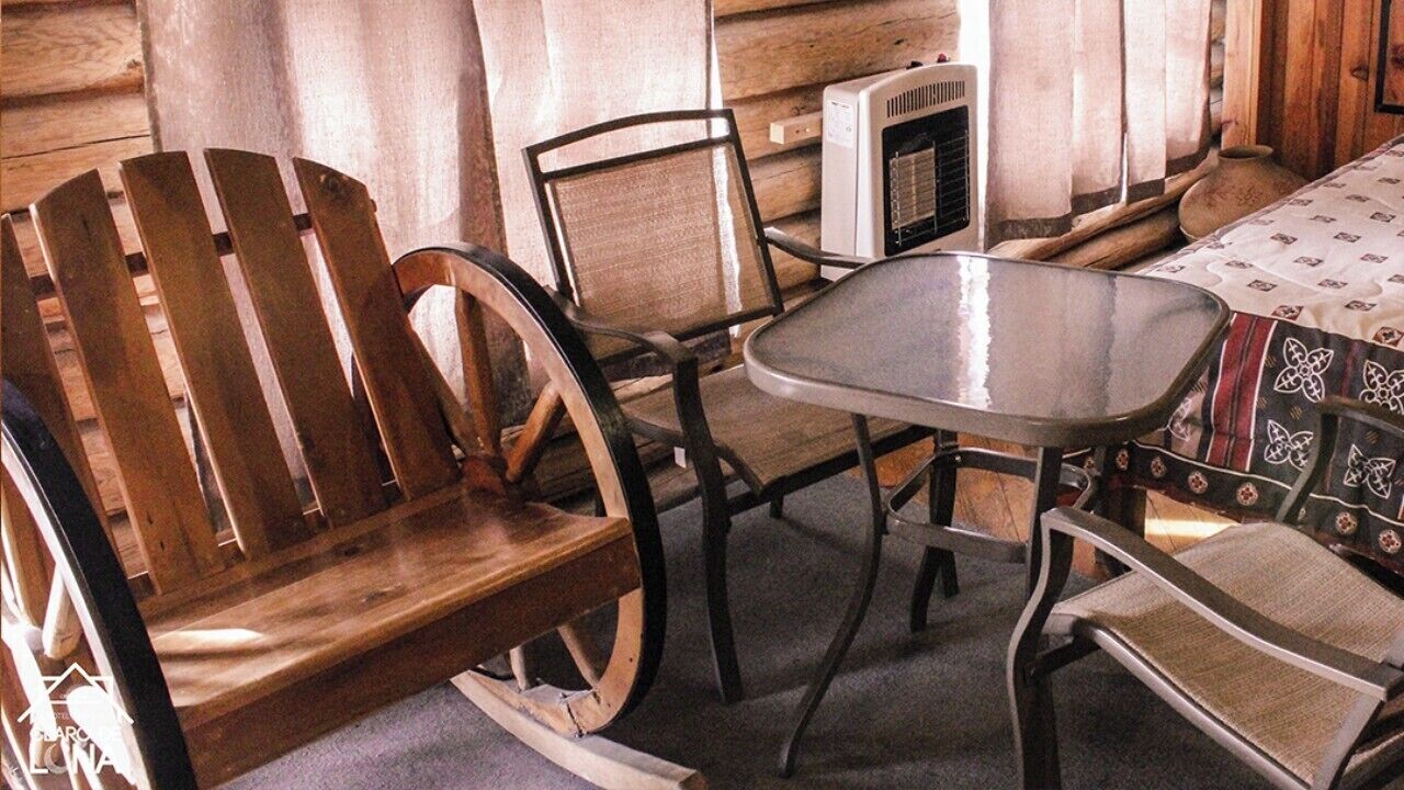 A rustic wooden interior with a wooden bench, a metal table, and a patterned tablecloth.