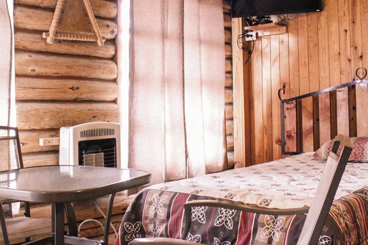 Una habitación tipo cabaña de madera con una cama, una mesa y una silla.
