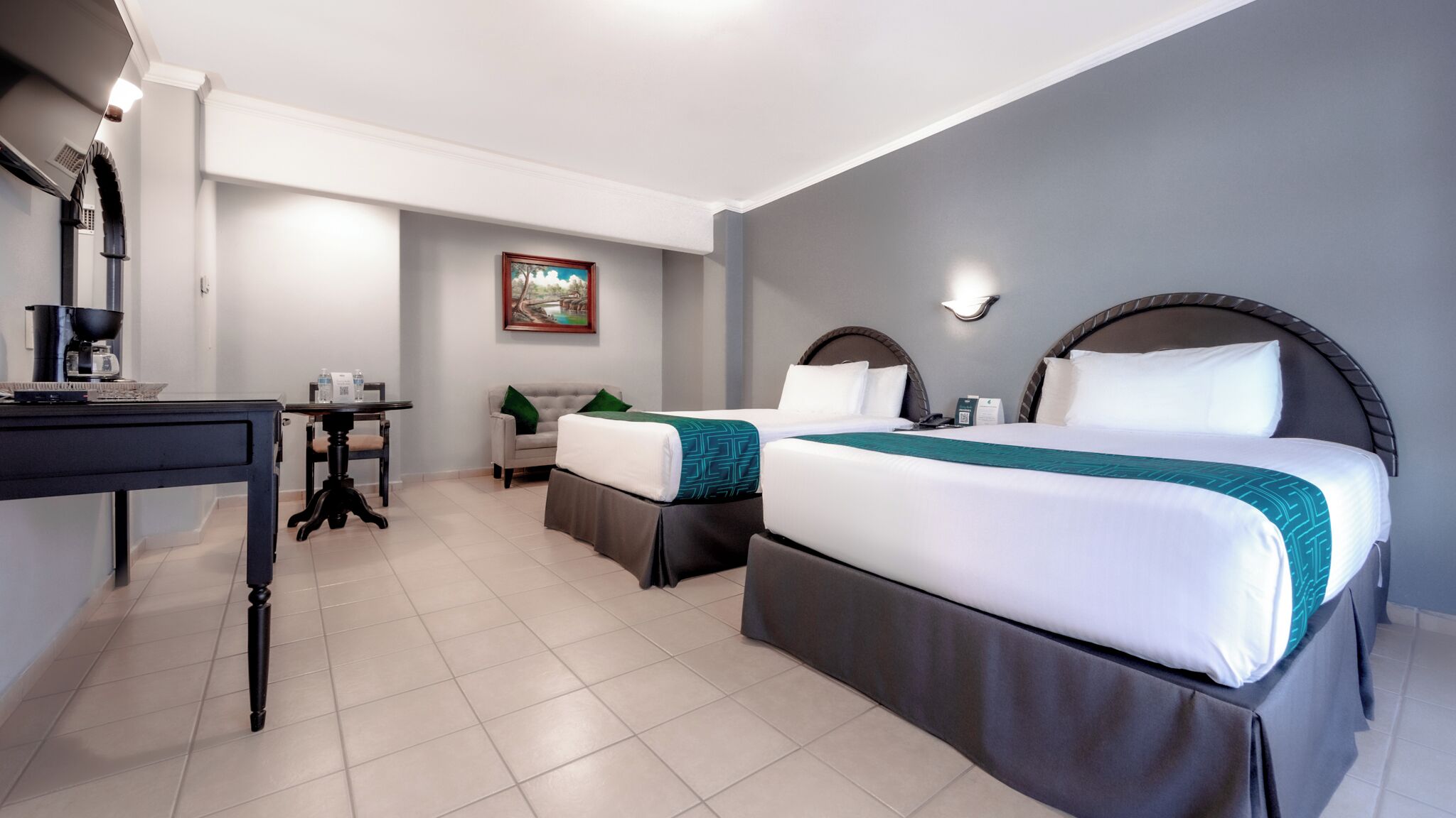 Une chambre d’hôtel avec deux lits, un bureau doté d’une machine à café, une chaise et un tableau au mur.