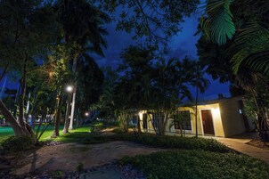 Vista nocturna de un resort con un camino iluminado, palmeras y un edificio con puerta y ventanas.