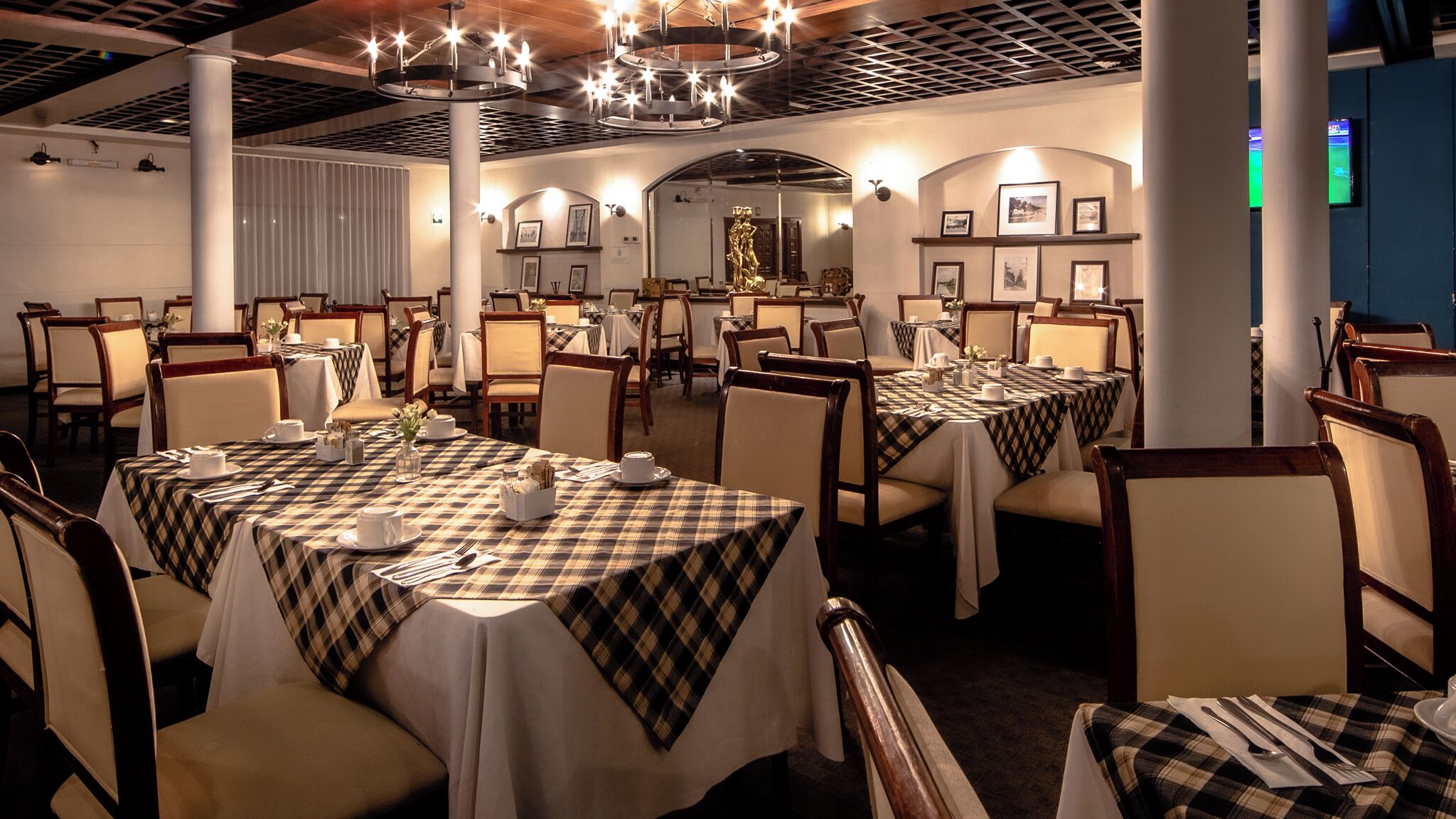 A dining area with multiple tables set for service, featuring checkered tablecloths and formal dining chairs.
