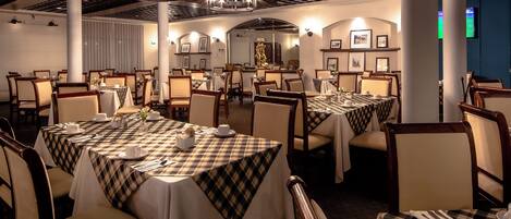 A dining area with multiple tables set for service, featuring checkered tablecloths and formal dining chairs.