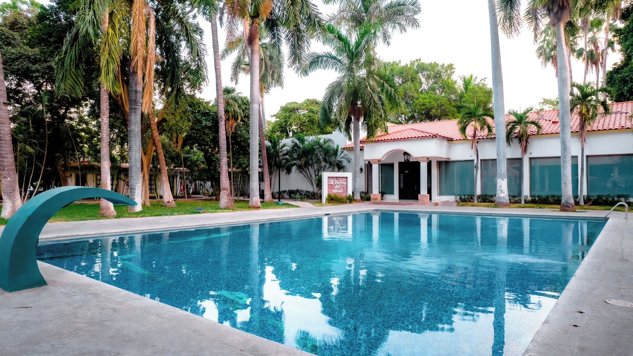 Una piscina rodeada de palmeras y un edificio con techo de tejas rojas.