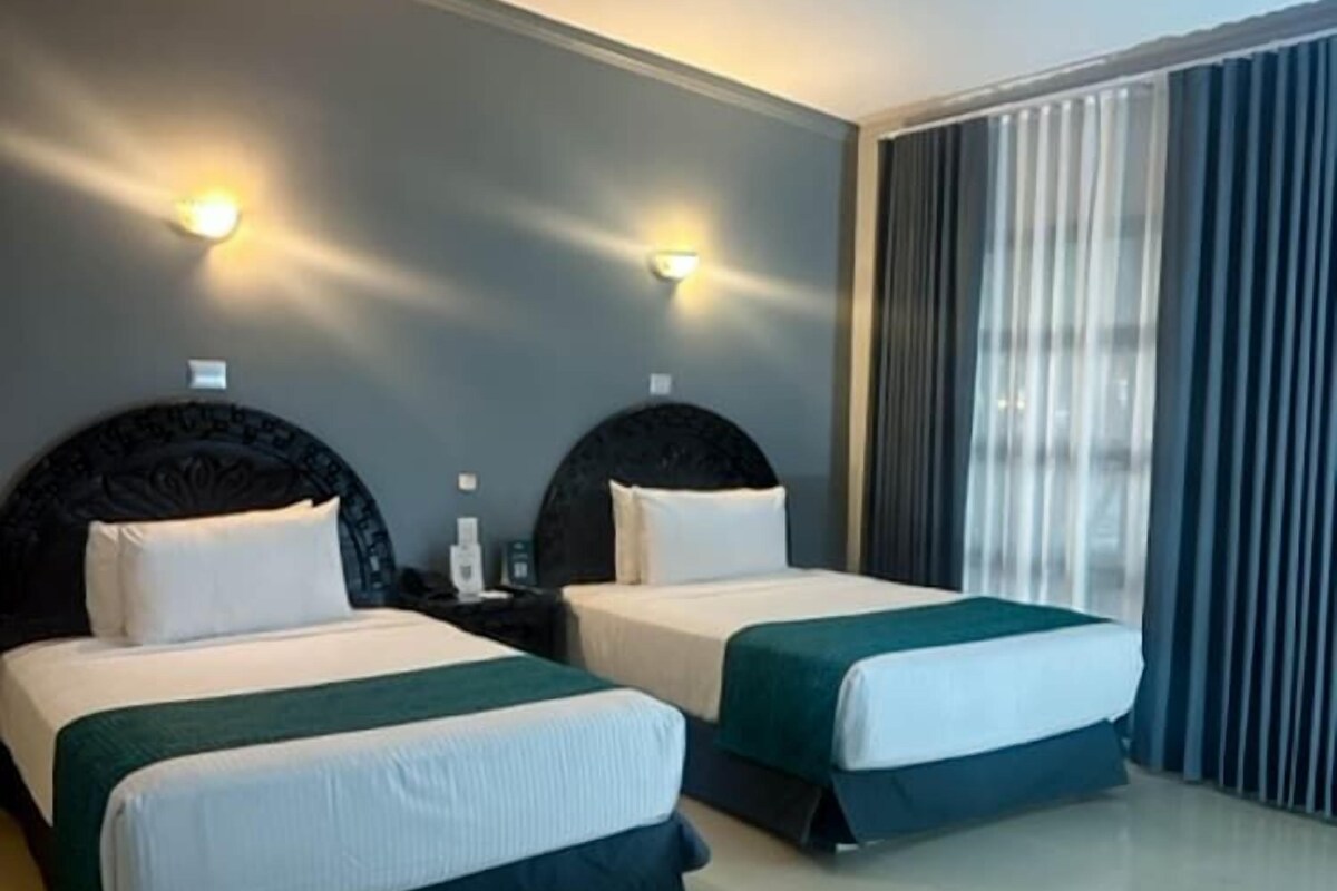 Habitación de hotel con dos camas, cada una con cabecera, mesita de noche y lámpara de pared.