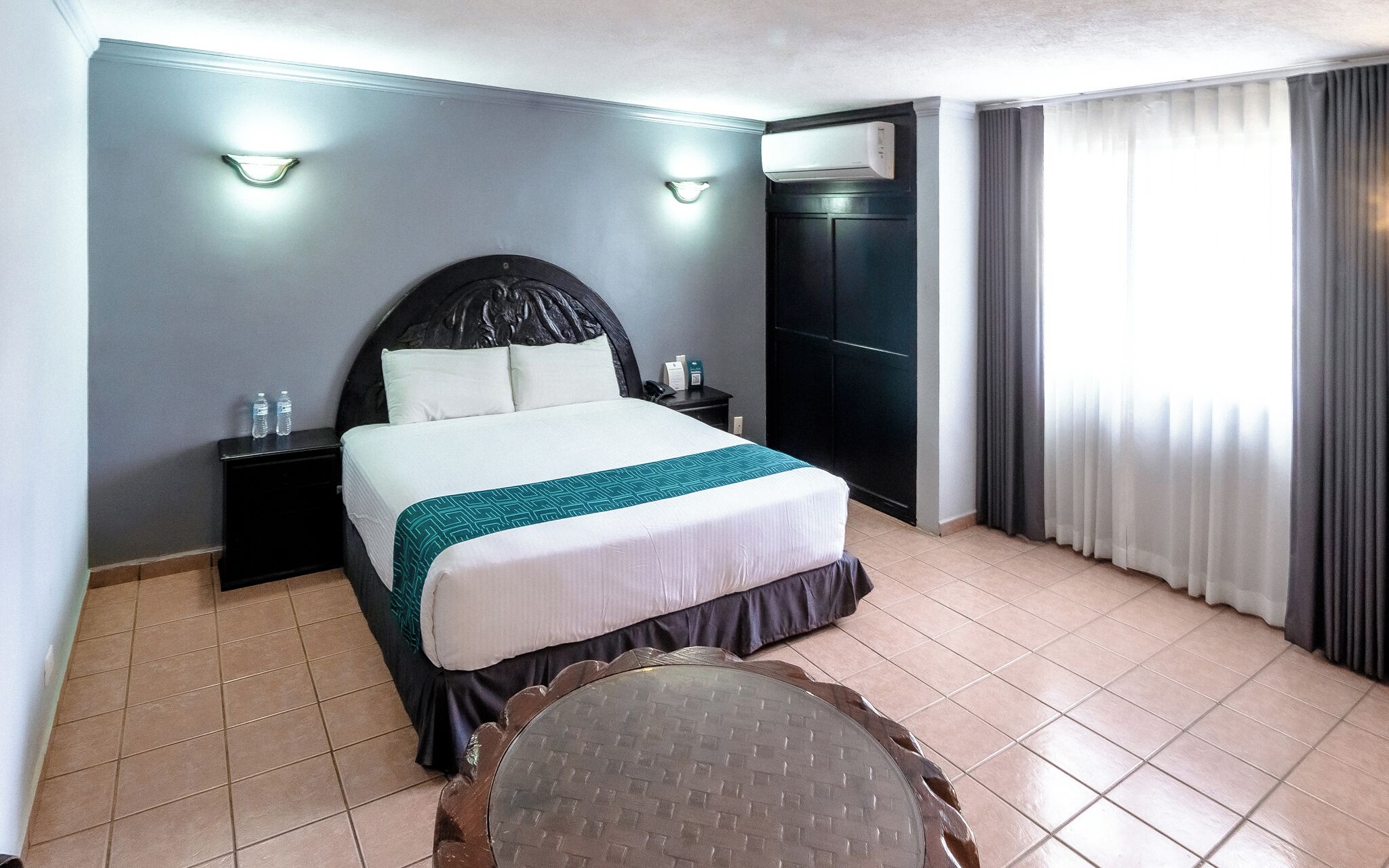 Une chambre d’hôtel avec un lit, des tables de chevet, une table ronde et une fenêtre avec des rideaux.