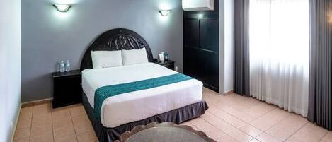 Une chambre d’hôtel avec un lit, des tables de chevet, une table ronde et une fenêtre avec des rideaux.