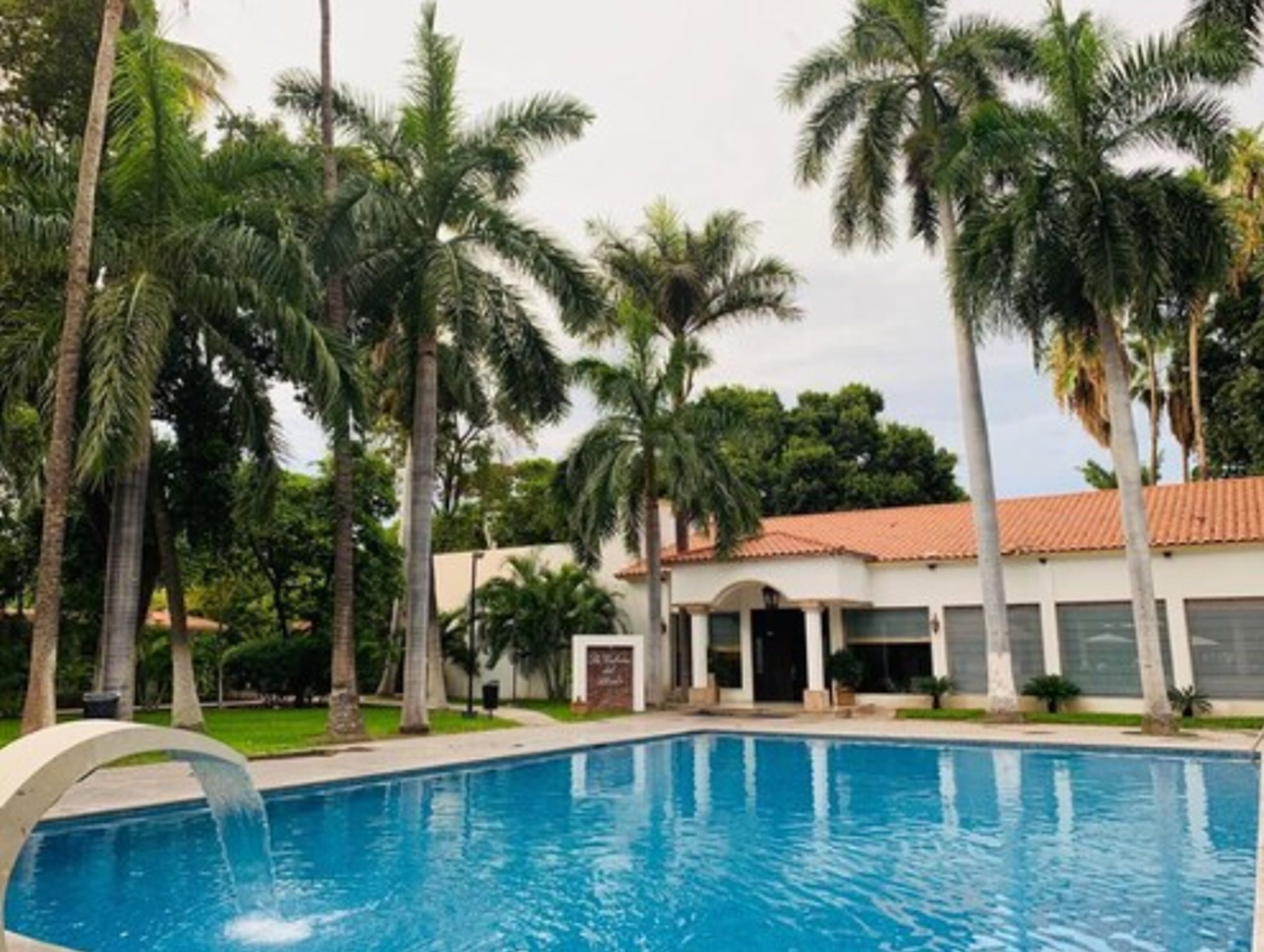 A swimming pool surrounded by palm trees and a building with a tiled roof.