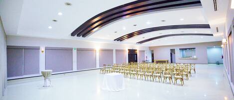 A large, modern conference room with rows of chairs and a central table, equipped with ceiling lights and a visible exit door.
