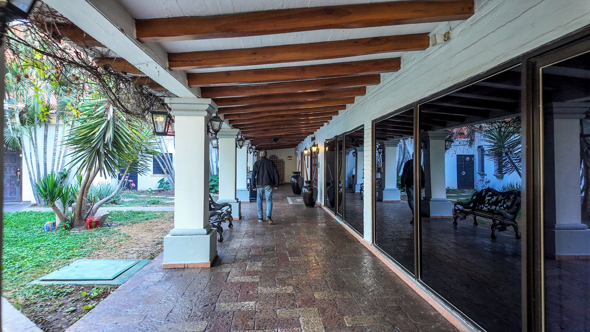 A covered walkway with wooden beams, a bench, and a large window reflecting the outside scene.