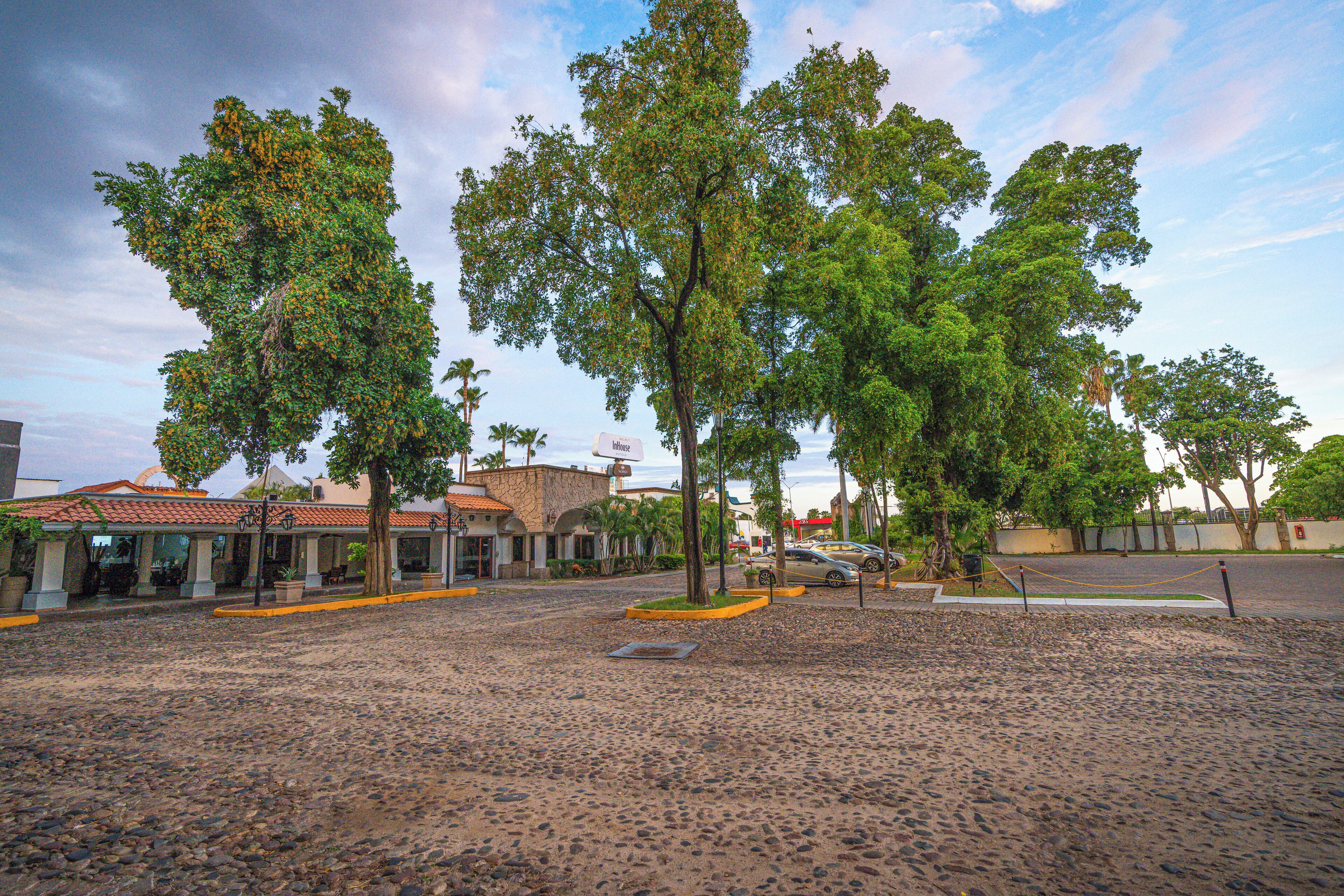 Una plaza adoquinada con árboles, un edificio con techo de tejas y un coche estacionado.