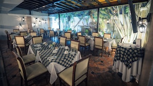 Un restaurante con varias mesas, sillas y una vista tropical a través de amplios ventanales.