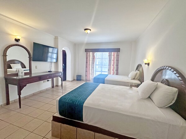 Habitación de hotel con una cama grande, una cama más pequeña, un escritorio con silla, un televisor y una ventana con cortinas.