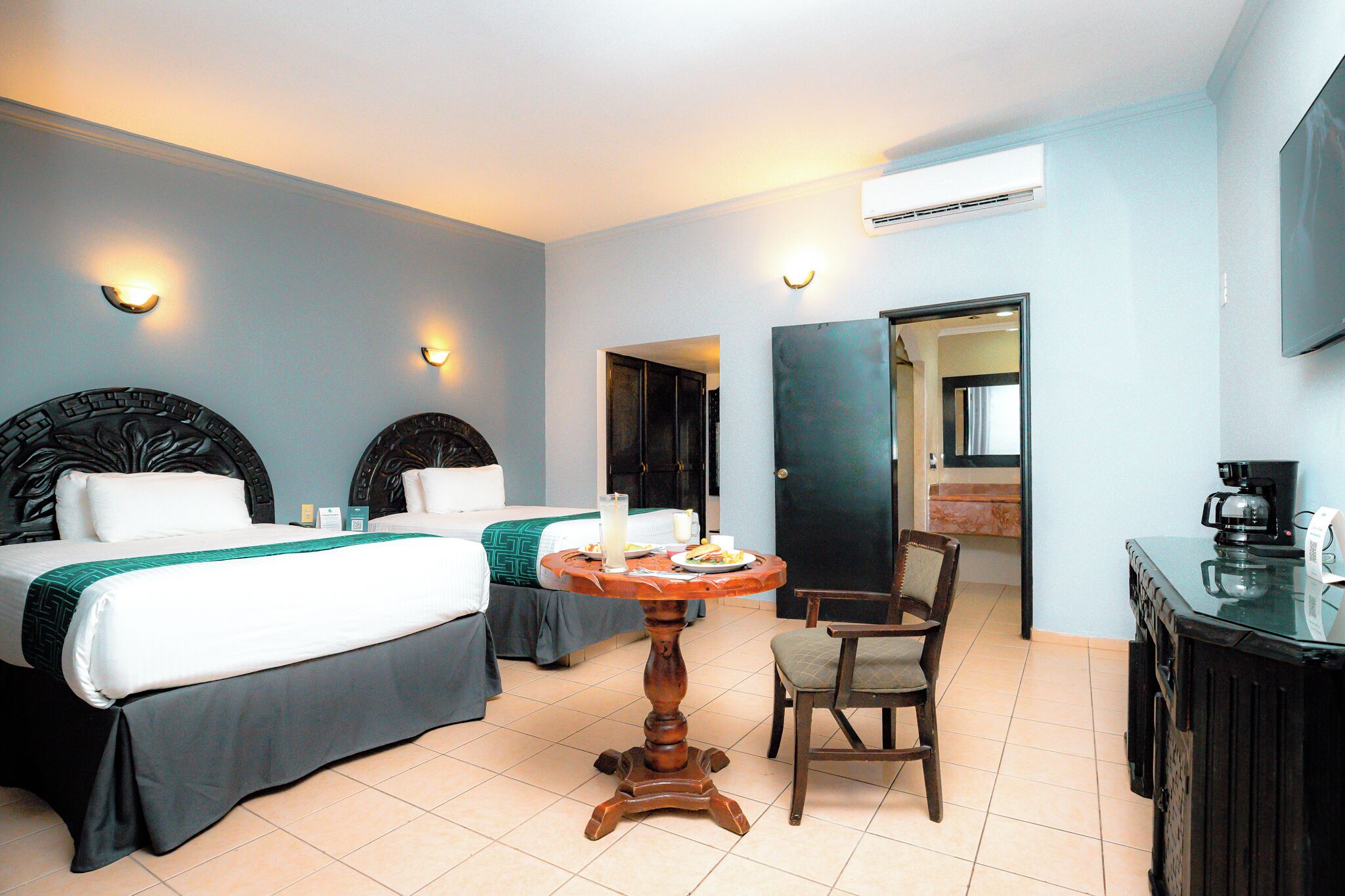 Habitación de hotel con dos camas, una mesa de comedor, una silla, una cafetera y un aire acondicionado.