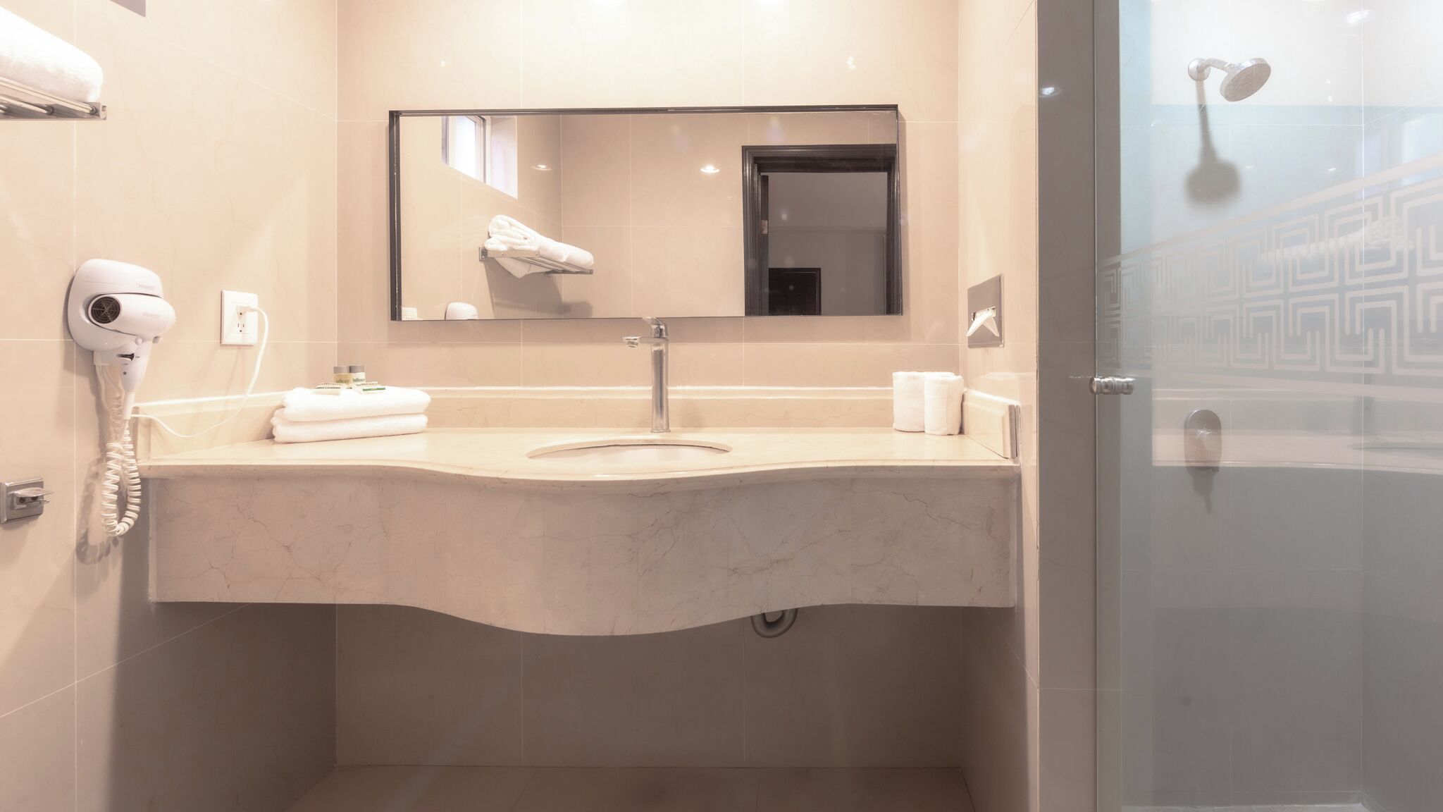 Un baño moderno con lavamanos de mármol, secador de pelo y cabina de ducha con paredes de cristal.