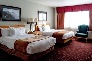 A hotel room with two beds, a desk, a chair, and a large window with curtains.