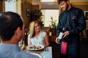 A restaurant interior with a dining table, chairs, and a waiter holding a bottle of wine. - Talkeetna Alaskan Lodge (Talkeetna)