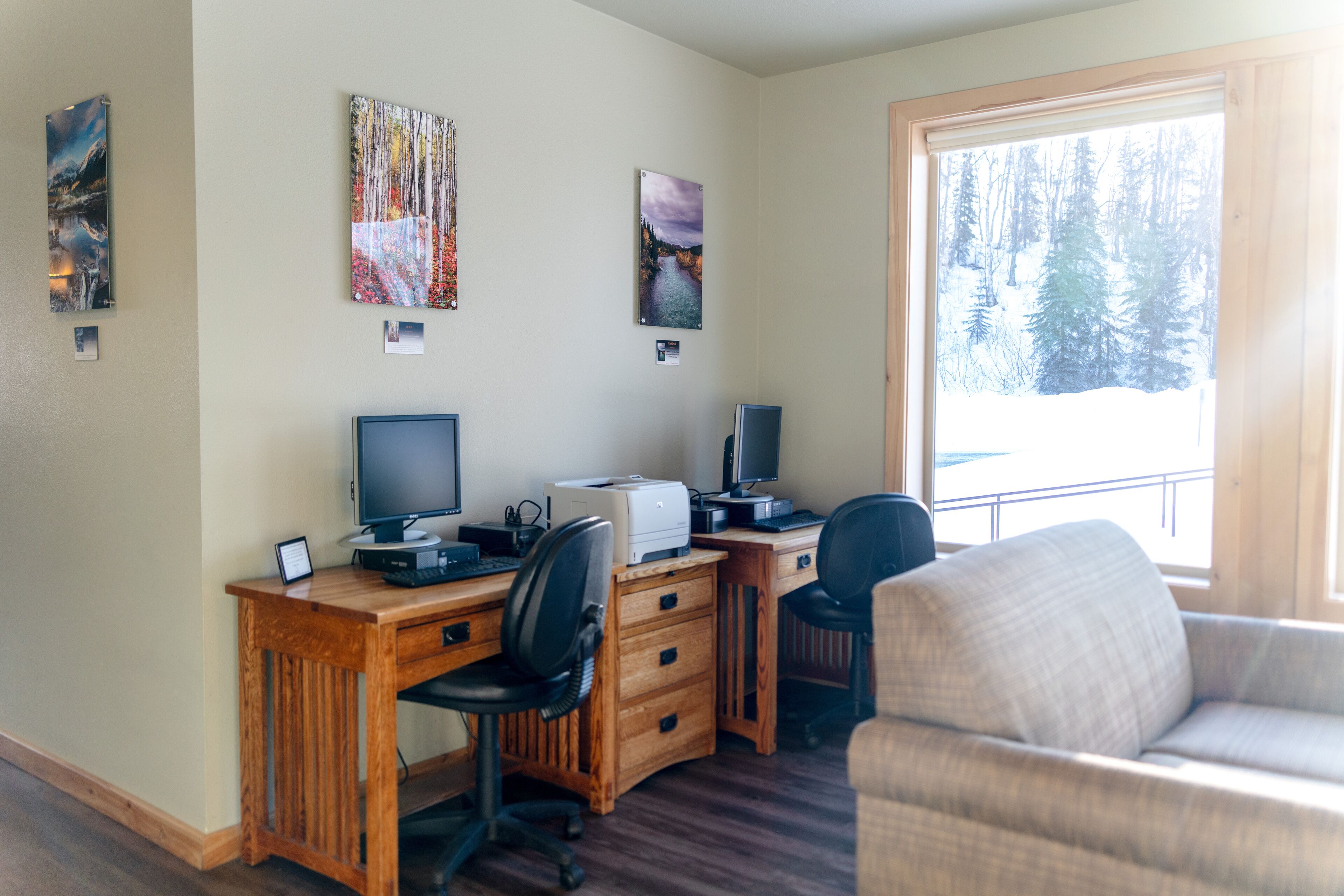 A room with a wooden desk, two monitors, a printer, and a couch.