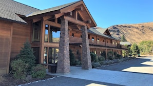 A large wooden lodge with a covered walkway, stone pillars, and a mountain backdrop. - The Lodge at Canyon River Ranch (Ellensburg)