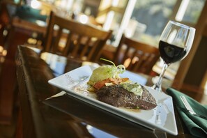 A plate of food with a glass of red wine on a table in a restaurant. - The Lodge at Canyon River Ranch (Ellensburg)
